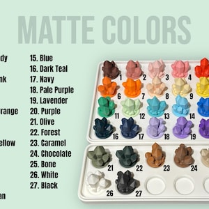Puede incluir: Una exhibici&oacute;n de objetos en forma de cristal de color mate en una bandeja blanca. La imagen presenta una carta de colores con 27 colores, incluyendo borgo&ntilde;a, rosa y azul. El texto "MATTE COLORS" est&aacute; en la parte superior.
