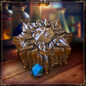 May include: A gold-colored, ornate dice tower with a sun-like face design. The tower is next to a blue and green multi-sided die. The image has the text "Tiny Towers" and "Fates End 3D Printables".