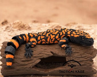 May include: A detailed, orange and black Gila monster figurine resting on a piece of driftwood. The lizard's body is segmented, with a pattern of orange blotches and stripes on a black base. The figurine has small, detailed black feet and a black head.