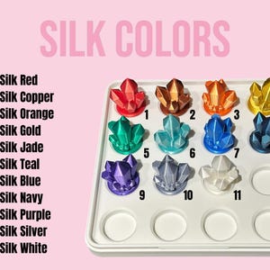 Puede incluir: Una bandeja blanca con 11 peque&ntilde;os recipientes en forma de cristal llenos de pinturas de seda de diferentes colores. Los colores son rojo, cobre, naranja, oro, jade, azul verdoso, azul, azul marino, morado, plata y blanco. La bandeja est&aacute; etiquetada como "Silk Colors" y cada recipiente est&aacute; numerado del 1 al 11.