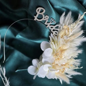 May include: A white and beige floral headband with a silver 'Bride' headband with rhinestones.