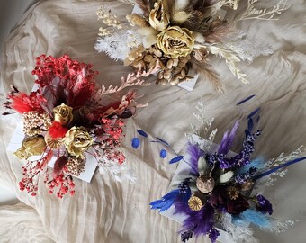 May include: Three dried flower arrangements in white boxes. One arrangement features red, gold, and white flowers. Another has beige and gold tones. The third arrangement is composed of purple and blue flowers.