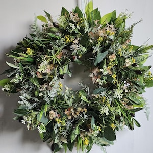 May include: A green and brown wreath made of artificial greenery, including leaves, ferns, and small flowers. The wreath is decorated with small black berries.