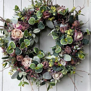 Può includere: Una ghirlanda verde lussureggiante con fiori rosa e bordeaux, foglie di eucalipto e bacche. La ghirlanda è perfetta per un arredamento autunnale o invernale.