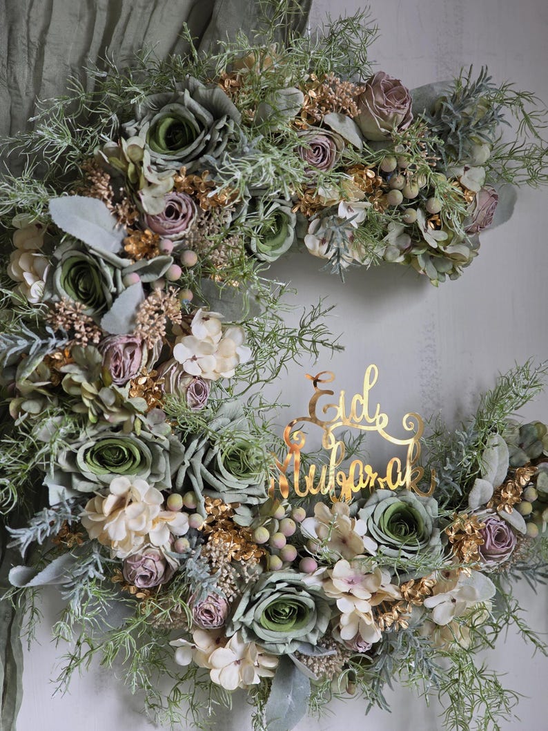 May include: A crescent-shaped floral wreath with green, cream, and mauve roses, complemented by gold-coloured foliage and berries. A gold script reads "Eid Mubarak". This decorative piece is suitable for celebrations.