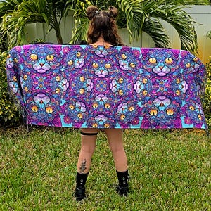 May include: A purple and blue tapestry with a repeating pattern of cat faces. The tapestry is fringed and has a psychedelic design.