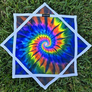 May include: A square, tie-dye textile with a spiral design in vibrant colors including blue, yellow, orange, and purple. The textile is framed by a white, star-shaped border. The text "PERFECT VISION" is visible.
