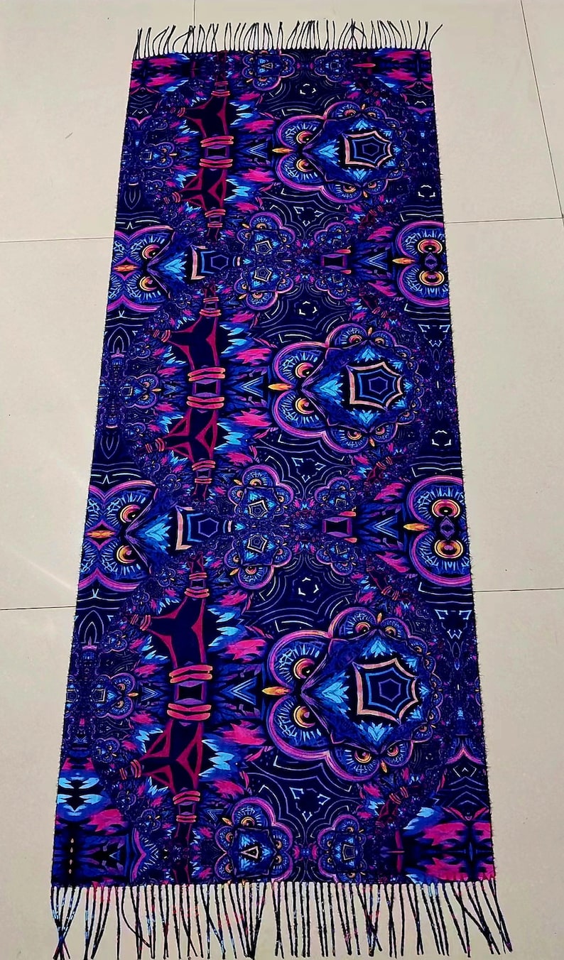 May include: A long, rectangular scarf with a dark blue background and a colourful, intricate pattern of owls and geometric shapes. The scarf has a fringe on both ends.