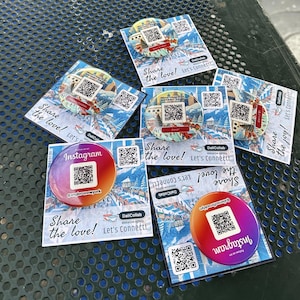 May include: A collection of eight round, colorful buttons with QR codes and the text "Share the love!" and "Share the joy!" printed on them. The buttons are arranged on a green metal surface.