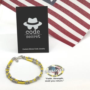 May include: A double-strand bracelet featuring alternating yellow seed beads and silver-toned metallic beads. A black display card shows a white hat icon, the text code secret, and Custom Morse Code Jewelry. A circular logo features a soldier silhouette.