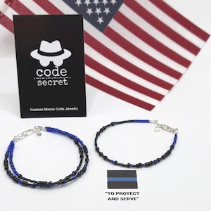 May include: Two bracelets made of small black and blue beads with silver-toned clasps. One bracelet is a double-strand design, while the other is a single strand. A black card displays the text code secret Custom Morse Code Jewelry.