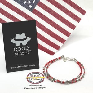 May include: A double-strand bracelet featuring small red beads and silver-toned metallic cylinders arranged in a pattern. Beside it is a black card with a hat icon and the text code secret Custom Morse Code Jewelry and a circular R.E.D. logo.