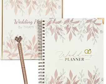 May include: A white wedding planner with a gold spiral binding and a floral design. The cover features the text "Wedding Planner" and a gold ring design. The planner comes with a rose gold pen with a heart-shaped top.