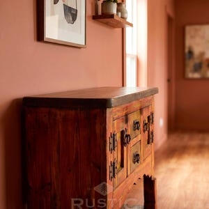 May include: A rustic wooden cabinet with a dark stained top and a distressed, multi-colored finish. The cabinet features multiple drawers and doors with ornate metal hardware. The "Rustic Expressions" logo is visible on the front.