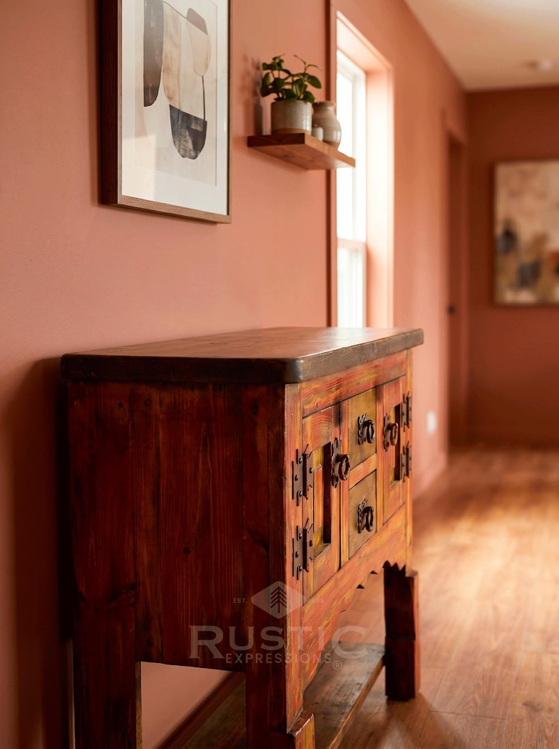 May include: A rustic wooden cabinet with a dark stained top and a distressed, multi-colored finish. The cabinet features multiple drawers and doors with ornate metal hardware. The "Rustic Expressions" logo is visible on the front.