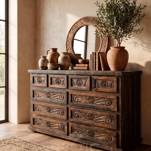 May include: A rustic wooden dresser with carved drawer fronts and a dark finish. The dresser is topped with a round mirror, pottery, books, and a potted plant. The room has a warm, inviting atmosphere.