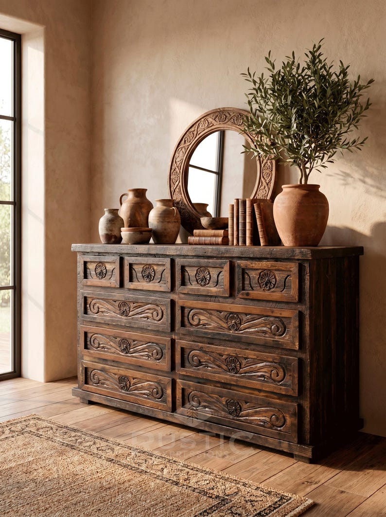May include: A rustic wooden dresser with carved drawer fronts and a dark finish. The dresser is topped with a round mirror, pottery, books, and a potted plant. The room has a warm, inviting atmosphere.