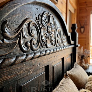Pu&ograve; includere: Primo piano di una testiera in legno intagliato marrone scuro. La testiera presenta un motivo floreale con dettagli intricati e una finitura invecchiata. Il telaio del letto &egrave; parzialmente visibile, con cuscini e biancheria da letto.