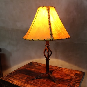 May include: A rustic table lamp with a twisted metal base and a leather lampshade. The lampshade is a light yellow color and has a stitched edge.