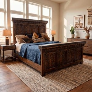 May include: A bedroom featuring a large, intricately carved wooden bed frame with a matching headboard and footboard. The bed is adorned with pillows and a blue blanket. The room includes a rug, nightstands, lamps, and a dresser.