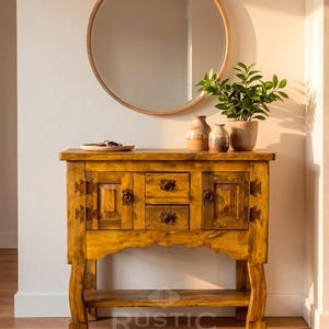 May include: A rustic wooden console table with two drawers and two cabinet doors, adorned with decorative hardware. A round mirror hangs above the table, and a small plant and vases sit on top. The table is made of light brown wood and has a lower shelf.