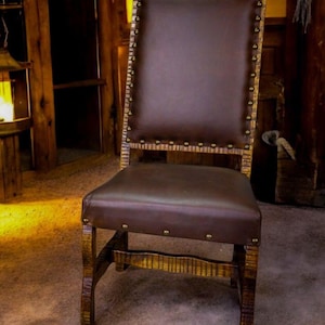 May include: A rustic wooden chair with a brown leather seat and back. The chair has a high back and is decorated with metal studs. The chair is sitting on a wooden floor.