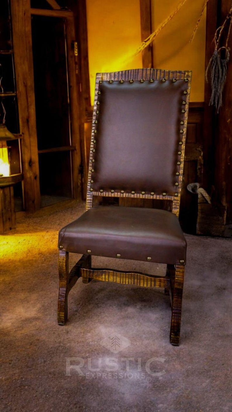 May include: A rustic wooden chair with a brown leather seat and back. The chair has a high back and is decorated with metal studs. The chair is sitting on a wooden floor.