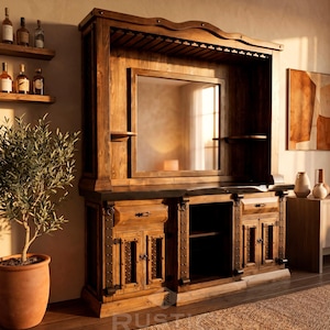May include: A large, rustic wooden entertainment center with a built-in mirror and storage cabinets. The dark brown wood is accented with metal hardware. A small olive tree in a terracotta pot and a woven rug are in the foreground.