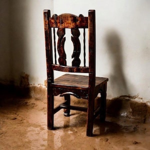 Puede incluir: Una silla de madera marr&oacute;n oscuro con respaldo tallado y un asiento simple. La silla est&aacute; sentada en un suelo de tierra.