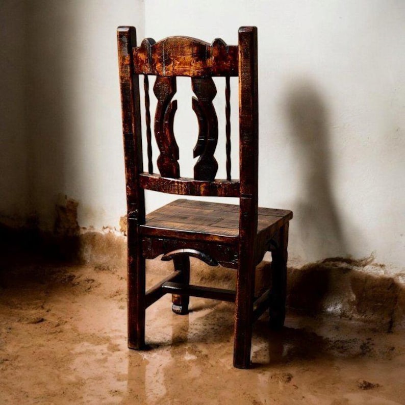 Puede incluir: Una silla de madera marr&oacute;n oscuro con respaldo tallado y un asiento simple. La silla est&aacute; sentada en un suelo de tierra.