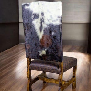 May include: A wooden dining chair with a brown leather seat and a cowhide back. The chair has a carved design on the legs and back.