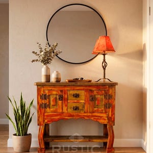 May include: A rustic, hand-painted wooden cabinet with drawers and doors, featuring warm orange and yellow tones. A round black mirror hangs above, with a lamp and decorative vases on top. A potted snake plant and a woven rug complete the scene.