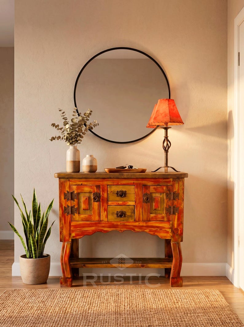 May include: A rustic, hand-painted wooden cabinet with drawers and doors, featuring warm orange and yellow tones. A round black mirror hangs above, with a lamp and decorative vases on top. A potted snake plant and a woven rug complete the scene.