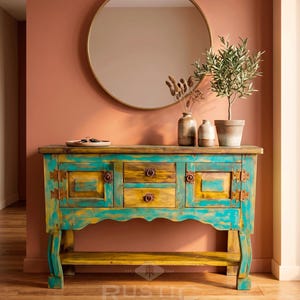 May include: A turquoise and yellow painted wooden console table with three drawers and two cabinet doors. A round gold mirror hangs above the table, which is decorated with vases and a potted plant. The table has a rustic design.