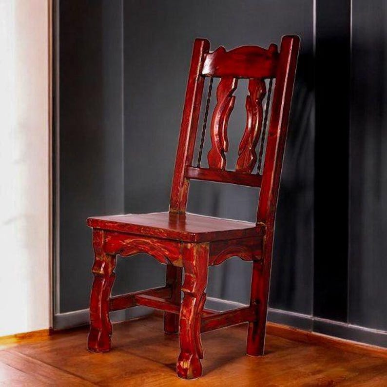 Puede incluir: Una silla de madera roja con respaldo tallado y acabado desgastado. La silla tiene un dise&ntilde;o sencillo con cuatro patas y un asiento.
