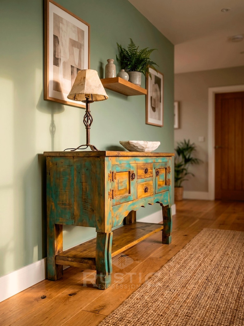 May include: A rustic, turquoise and yellow wooden cabinet with drawers and doors, topped with a lamp and a decorative bowl. The cabinet sits on a wooden floor, with a woven rug and framed artwork in the background.
