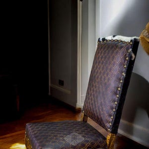May include: A brown leather dining chair with a diamond pattern and nailhead trim. The chair has a wooden frame and is sitting on a wooden floor. The chair is in a room with a white wall and a door in the background. The chair has a rustic design and is made by Rustic Expressions.