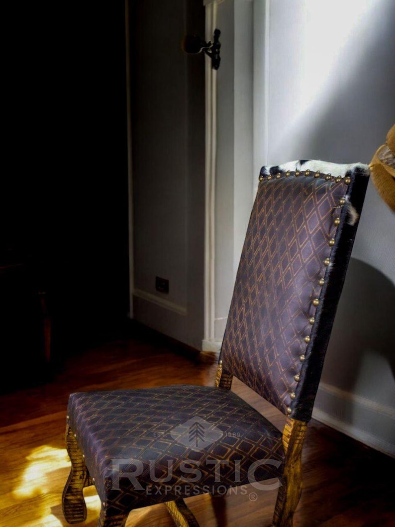 May include: A brown leather dining chair with a diamond pattern and nailhead trim. The chair has a wooden frame and is sitting on a wooden floor. The chair is in a room with a white wall and a door in the background. The chair has a rustic design and is made by Rustic Expressions.