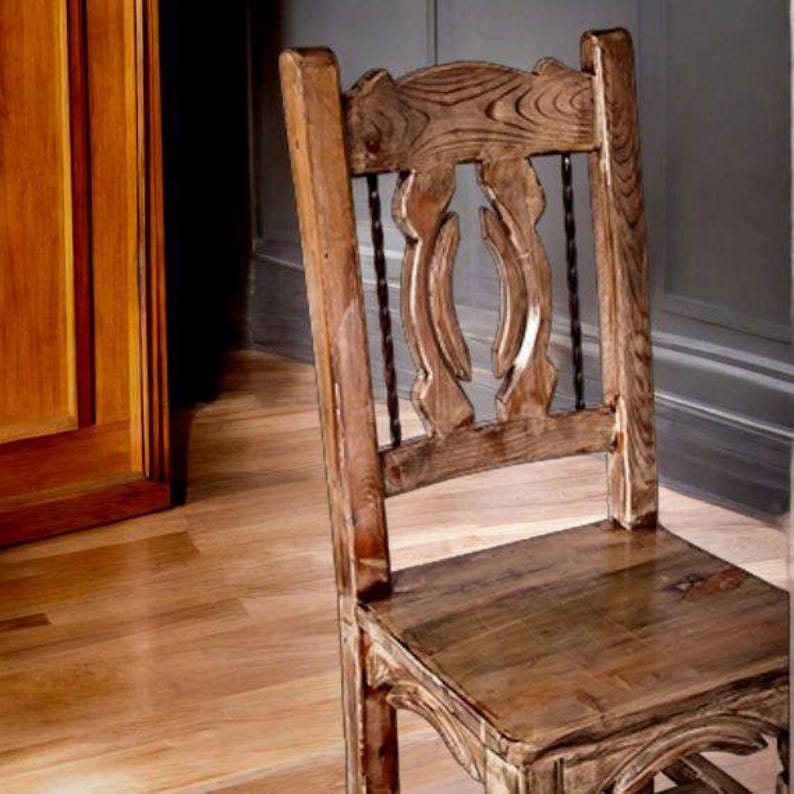 Puede incluir: Una silla de madera r&uacute;stica con respaldo tallado y asiento tejido. La silla est&aacute; hecha de madera natural con un acabado marr&oacute;n claro.