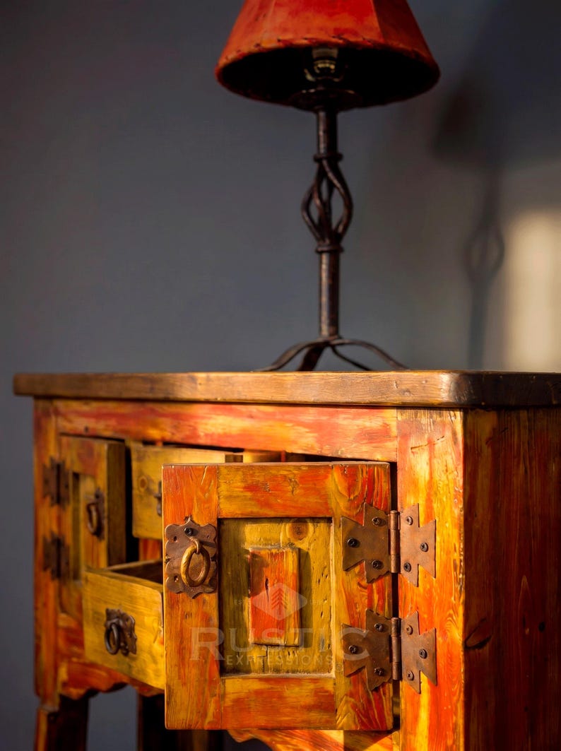 May include: A rustic wooden cabinet with an open drawer, painted in shades of yellow, orange, and red. The cabinet has metal hardware and a matching lamp with a red lampshade. The style is reminiscent of antique furniture.