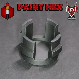 May include: A black 3D printed paint pot holder with four slots. The holder is designed to hold paint pots upright and prevent them from tipping over.