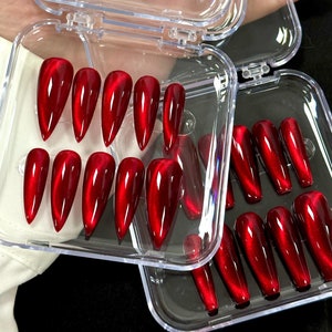 Könnte beinhalten: Ein Set mit 24 roten Stiletto-Kunstnägeln mit Katzenaugen-Effekt, verpackt in zwei durchsichtigen Plastikboxen.
