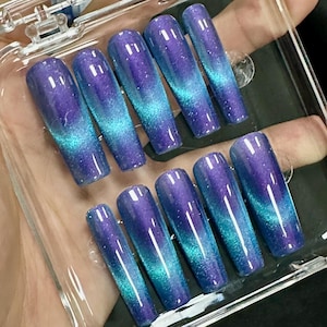 May include: A set of ten long, coffin-shaped false nails with a blue and purple ombre glitter finish. The nails are arranged in a clear plastic case.