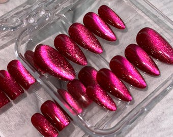 Puede incluir: Un juego de uñas postizas con acabado ojo de gato en color magenta intenso y un efecto magnético brillante y reflectante. Las uñas tienen forma de almendra puntiaguda y están dispuestas en un estuche de almacenamiento rectangular de plástico transparente.