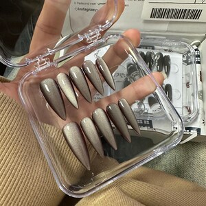 Peut inclure: Un &eacute;tui en plastique transparent contenant un jeu d'ongles postiches longs, en forme d'amande, de couleur taupe. Les ongles ont une finition chatoyante et sont dispos&eacute;s en rang&eacute;e dans l'&eacute;tui.