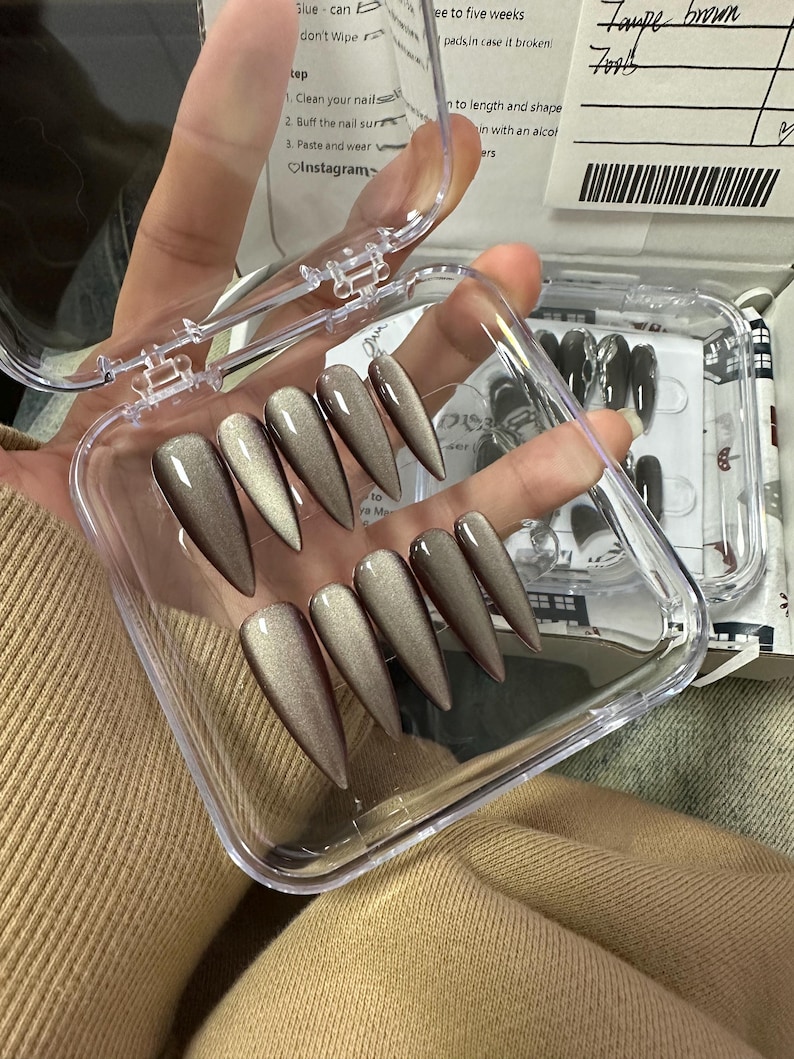 Peut inclure: Un &eacute;tui en plastique transparent contenant un jeu d'ongles postiches longs, en forme d'amande, de couleur taupe. Les ongles ont une finition chatoyante et sont dispos&eacute;s en rang&eacute;e dans l'&eacute;tui.