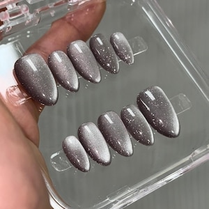 May include: A set of ten gray and silver ombre press-on nails with a glitter finish in a clear plastic case.