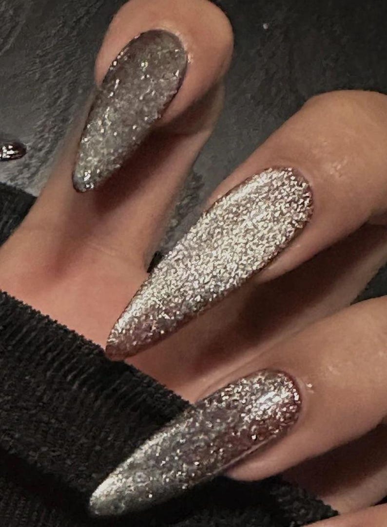 Peut inclure: Gros plan sur des ongles longs et pointus avec un vernis &agrave; ongles ombr&eacute; argent&eacute; paillet&eacute;. Les ongles sont peints avec un d&eacute;grad&eacute; de paillettes argent&eacute;es, partant d'une teinte plus fonc&eacute;e &agrave; la base et s'estompant vers une teinte plus claire &agrave; la pointe.