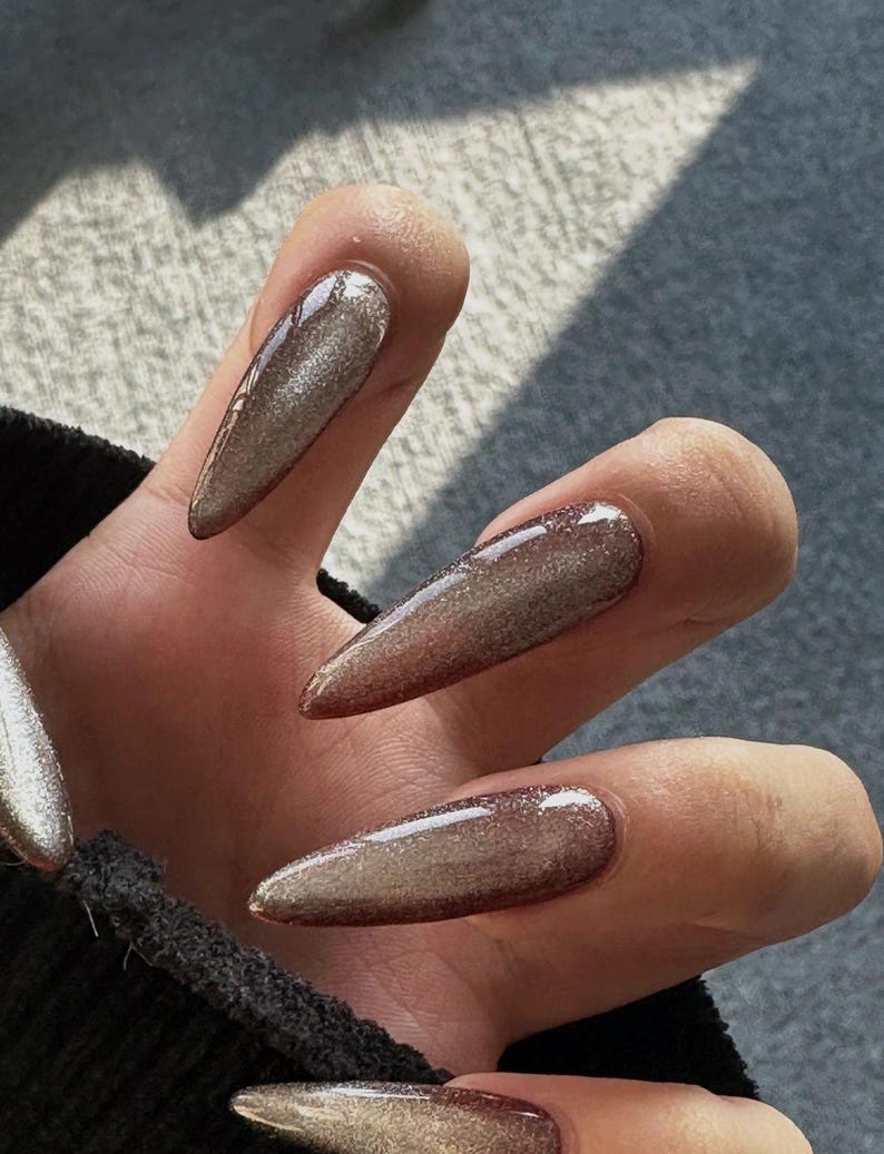 Peut inclure: Gros plan sur une main avec de longs ongles en forme de stiletto peints avec un vernis &agrave; paillettes argent&eacute; iris&eacute; chatoyant.