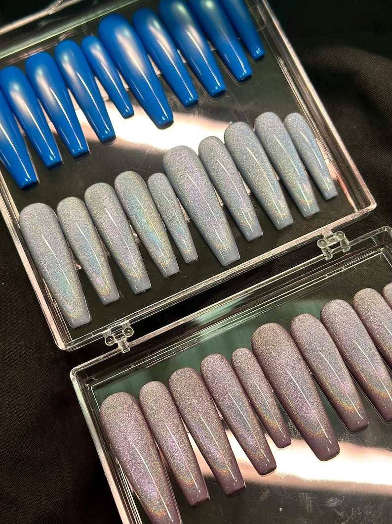 K&ouml;nnte beinhalten: Ein Set aus langen, sargf&ouml;rmigen Press-on-N&auml;geln, die in einer durchsichtigen Kunststoffbox angeordnet sind. Die Kollektion umfasst einfarbige, leuchtend blaue N&auml;gel sowie hellgraue und malvenfarbene holografische Glitzern&auml;gel in verschiedenen Gr&ouml;&szlig;en.